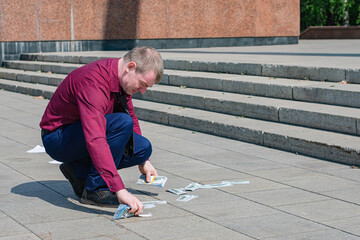 A businessman in a tie picks up a large amount of spilled money from the road