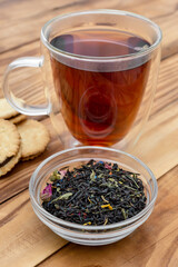 Glass bowl with dry tea leaves and cup of tea on the table. Close up.