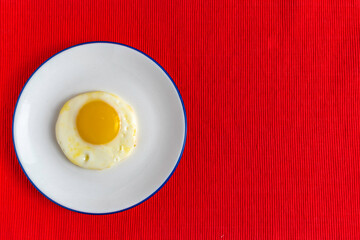 Plate with sunny side up egg for simple breakfast over red background. Free space for text.