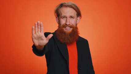 No stop. Serious redhead man say No, hold palm folded crossed hands in stop danger gesture, warning of finish, prohibited access, declining communication, body language. Young guy on orange background