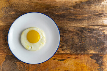 Sunny side up egg on ceramic plate over wooden background.