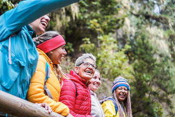 Multiracial women having fun exploring nature on trekking day in mountain forest - Focus on center...