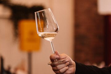 Glass of white wine held by a person at a premium wine tasting with friends and loved ones. - 545400652