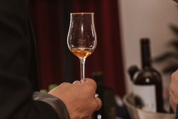 Glass of cognac held in hand at a presentation of selected drinks with friends and lovers of strong drinks.