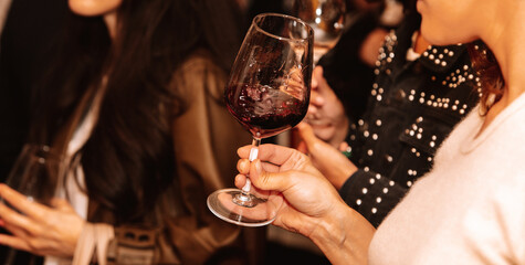 Glass of red wine held by a person at a premium wine tasting with friends and wine lovers.