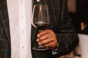 Glass of red wine held by a person at a premium wine tasting with friends and wine lovers.