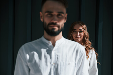 Man is in front of woman. Beautiful young couple is standing together against dark green background