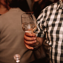 Glass of white wine held by a person at a premium wine tasting with friends and loved ones.