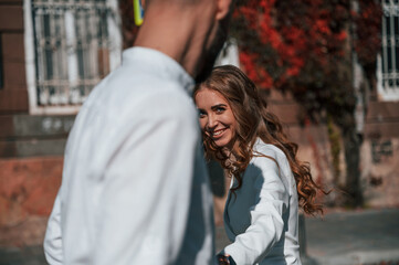 Having fun and holding each other by hands. Beautiful young couple is together on the street against old building