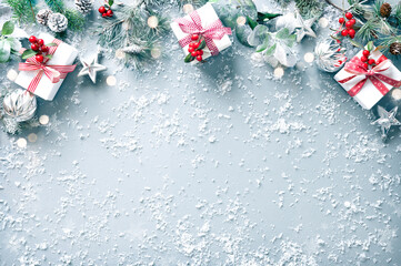 Winter fir branches, evergreen plants, berries, gift boxes and decorations on snowy background