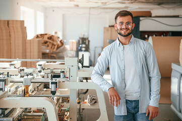 Handsome man is standing and smiling. Print house worker in white clothes is indoors