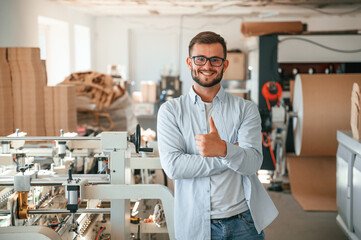 Handsome man is standing and smiling. Print house worker in white clothes is indoors