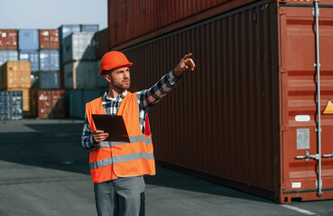 Giving instructions by the hand. Male worker is on the location with containers