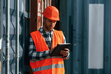 With digital tablet in hands. Male worker is on the location with containers