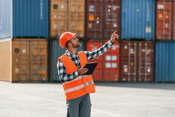 Giving instructions by the hand. Male worker is on the location with containers