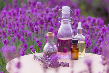 Obraz na płótnie Canvas A bottle of lavender essential oil on a wooden table and a field of flowers background.