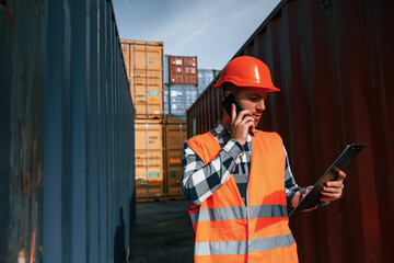 Having conversation by phone. Male worker is on the location with containers