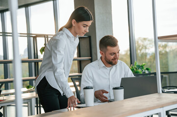 Using laptop. Man and woman are working in the modern office together