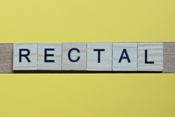 the gray word rectal of gray small wooden letters lies on a yellow table