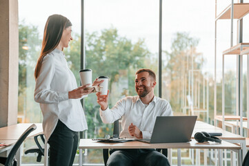 Cup with drinks in hands. Man and woman are working in the modern office together