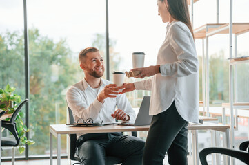 Obraz premium Cup with drinks in hands. Man and woman are working in the modern office together
