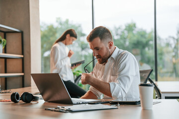 Fototapeta premium Sitting by the table white woman is at background. Employees are working in the modern office together