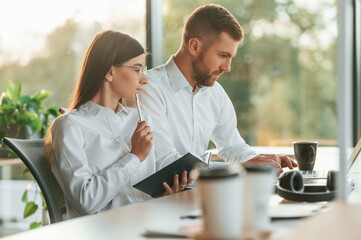 Working by using laptop. Man and woman are in the modern office together