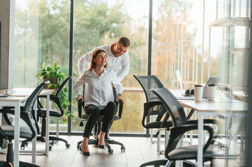 Fototapeta na wymiar Break time. Having fun. Riding a chair. Man and woman are working in the modern office together