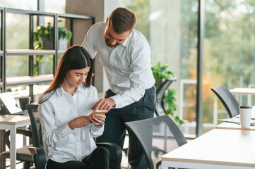 Pointing something in the smartphone. Man and woman are working in the modern office together