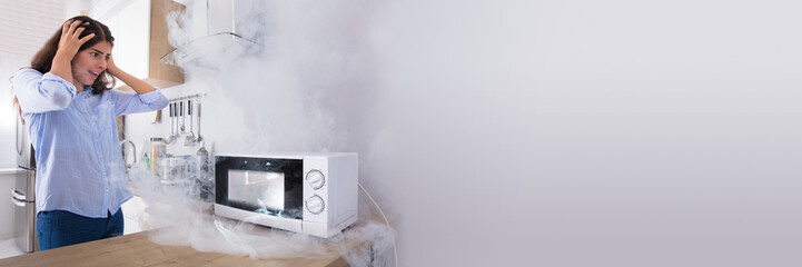 Unhappy Woman Looking At Smoke Emitting Through Microwave Oven