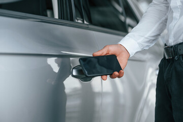 Opening the door. Young man in white clothes is in the car dealership