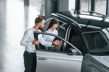 Fototapeta na wymiar Opening the door. Man with woman in white clothes are in the car dealership together