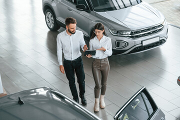 Top view. Man with woman in white clothes are in the car dealership together