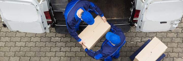 Two Delivery Men Unloading Cardboard Box From Truck