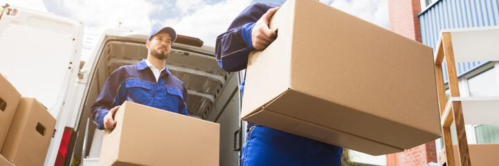 Close-up Of Two Delivery Men Carrying Cardboard Box