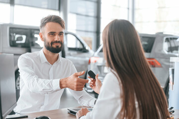 Automobile keys in hand. Man with woman in white clothes are in the car dealership together