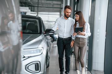Having a business conversation. Man with woman in white clothes are in the car dealership together
