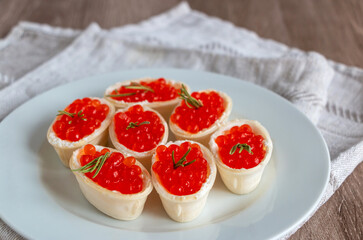 Red caviar in a waffle tartlet on a white plate with a linen napkin on a wooden background