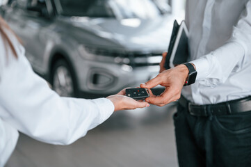 Obraz na płótnie Canvas Keys of new automobile. Close up view. Man with woman in white clothes are in the car dealership together