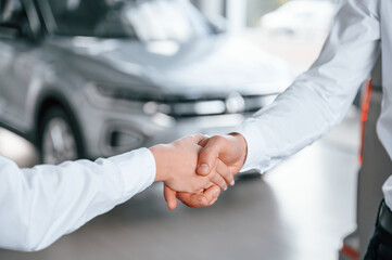 Close up view of handshake. Man with woman in white clothes are in the car dealership together