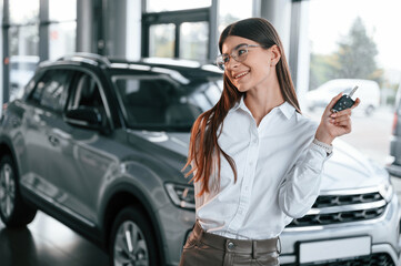 Holding keys. Young woman in white formal clothes is in the at dealership