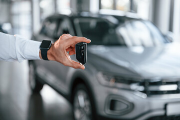 Close up view of keys that are in hand. Young man in white clothes is in the car dealership