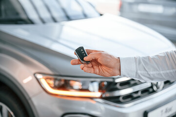 Keys and remote controller. Close up view. Young man in white clothes is in the car dealership