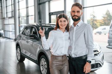 Fototapeta na wymiar Standing with keys in hands. Happy owners. Man with woman in white clothes are in the car dealership together