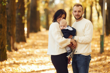 Two parents are having a walk with their little son in the autumn park