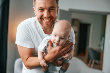 With baby in hands. Smiling, having fun. Father with toddler is at home, taking care of his son