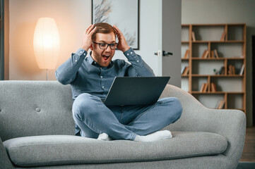 Celebrating success. Male freelance worker is using laptop at home. Cozy apartment