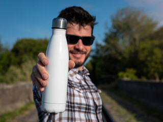 Hombre apuesto y sonriente mostrando botella metálica en blanco, para anuncios o propagandas....