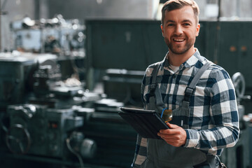 Standing and using graphic tablet. Factory male worker in uniform is indoors