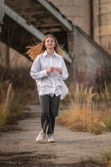 A young beautiful fair-haired girl in a light shirt runs across the wasteland.